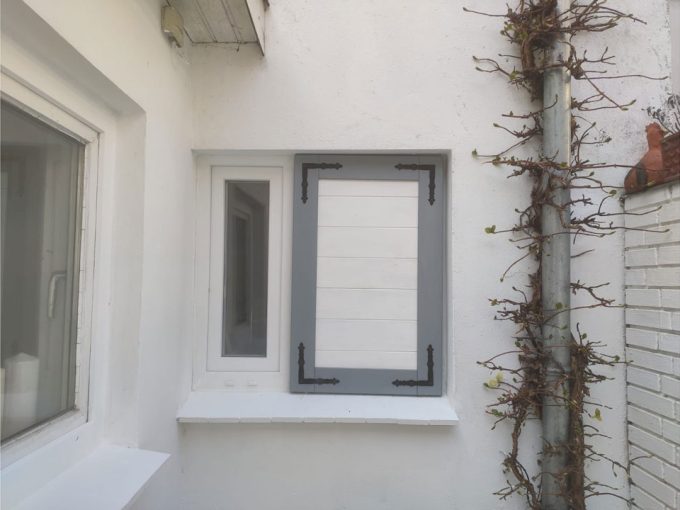 Ein Fenster mit weißen Fensterläden an einer weißen Wand.